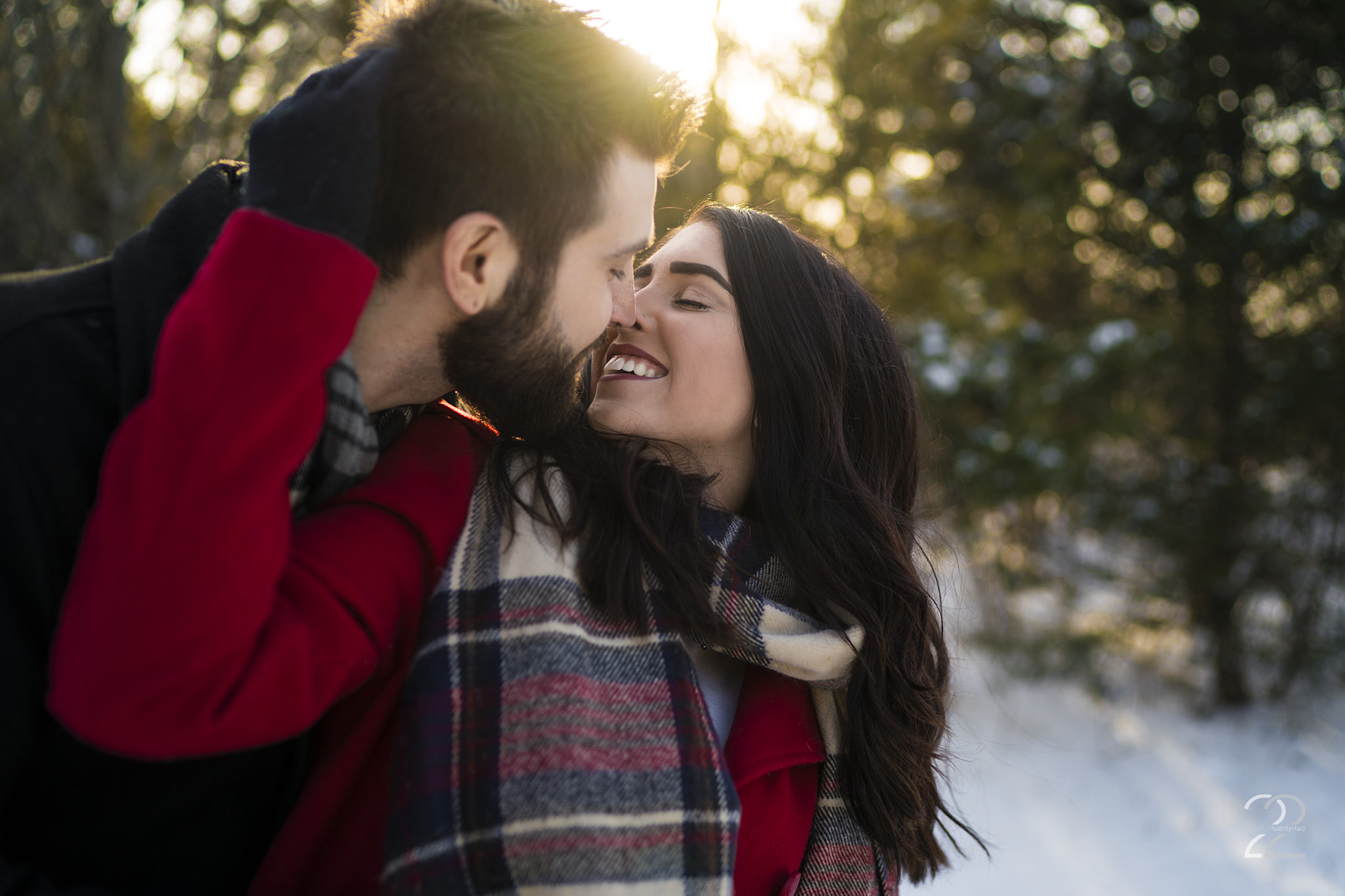 Woman pulls a man in for a kiss, both smiling, in the snow at sunset at Oakes Quarry Park by Dayton Wedding Photographer Studio 22 Photography